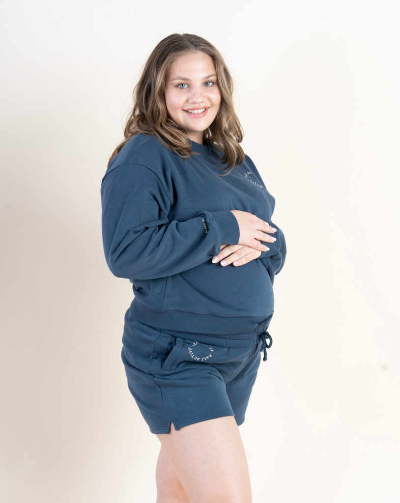 Beautiful pregnant model wearing blue color pullover and sweat shorts set with an affirmation be kind to yourself