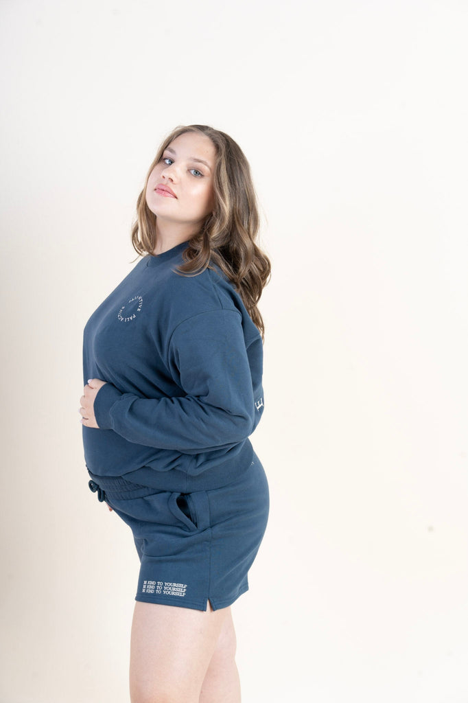 Beautiful pregnant model wearing blue color pullover and sweat shorts set with an affirmation be kind to yourself